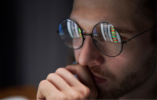 A person's glasses reflecting streams of dashboard data